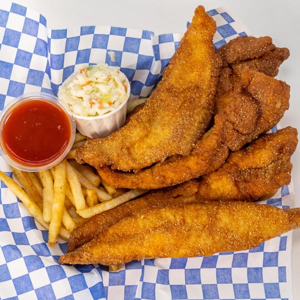 Fried fish fillets, french fries, coleslaw, and ketchup in a blue and white checkered paper basket.