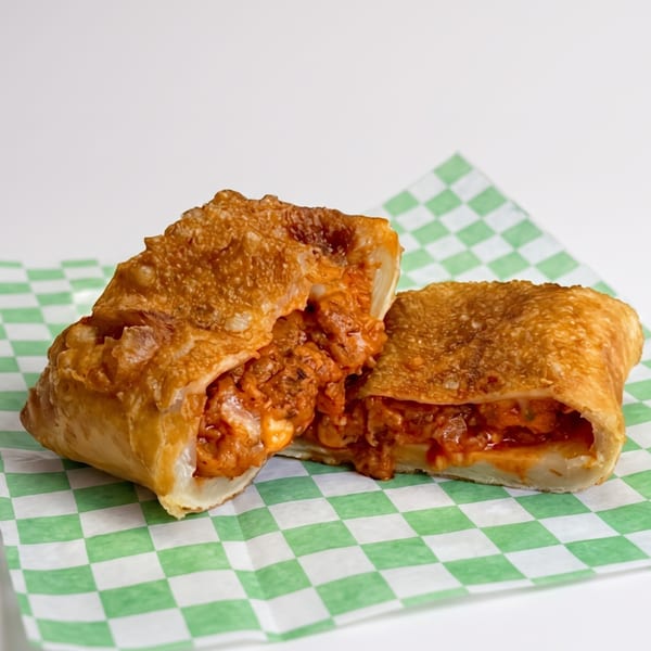 A golden-brown, crispy egg roll, cut in half, revealing a savory, cheesy, orange filling on checkered paper.