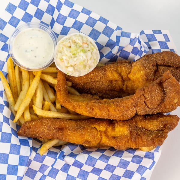 Fried fish fillets, french fries, coleslaw, and tartar sauce in a blue and white checkered basket.