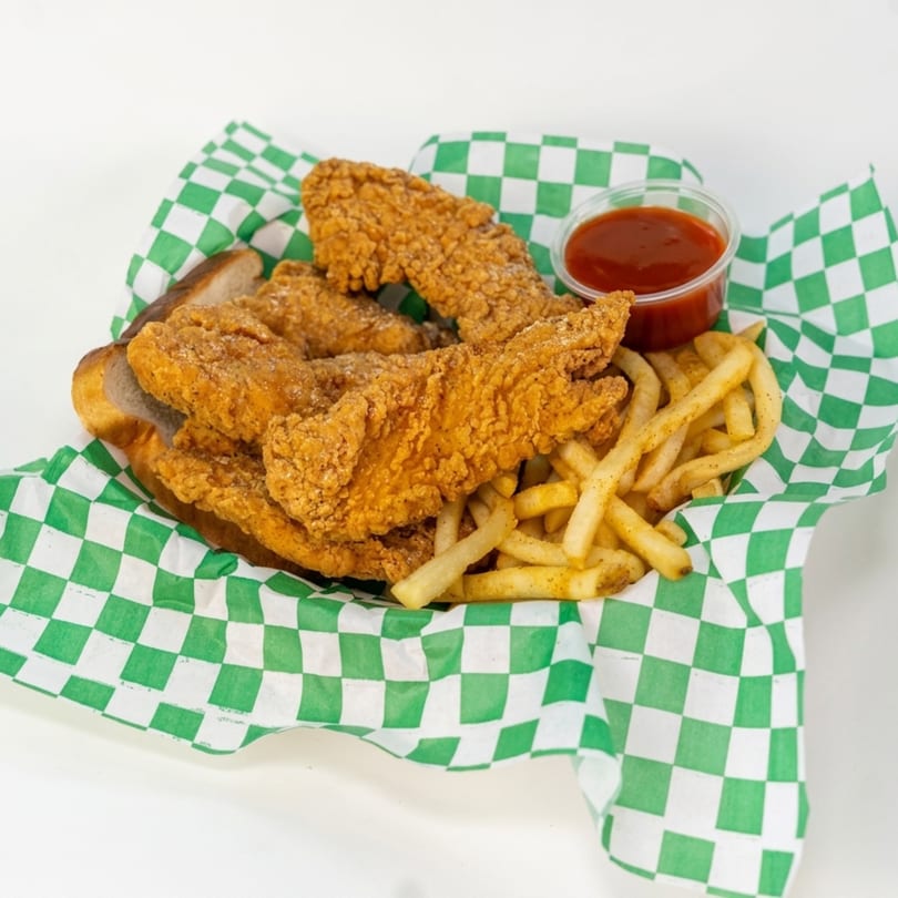 Crispy fried chicken tenders, french fries, and a side of ketchup in a green and white checkered basket.