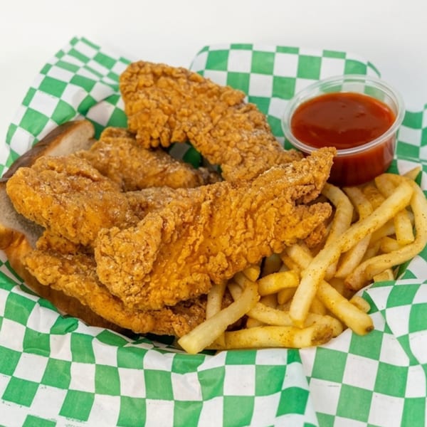 Crispy fried chicken tenders and french fries with a side of ketchup in a green checkered basket.