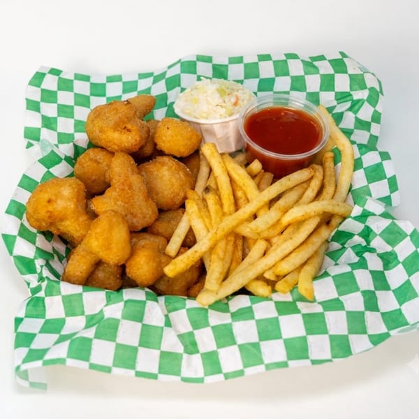 Basket of golden fried bites and French fries with coleslaw and red dipping sauce on green-and-white checkered paper.